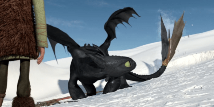 Toothless, the black Night Fury dragon, standing on a snowy hillside with his artificial tail fin extended while Hiccup stands partially in front of him.
